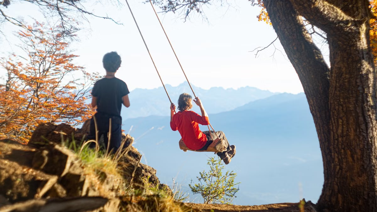 Two children playing on a swing in the scenic outdoors of El Bolsón, Argentina.